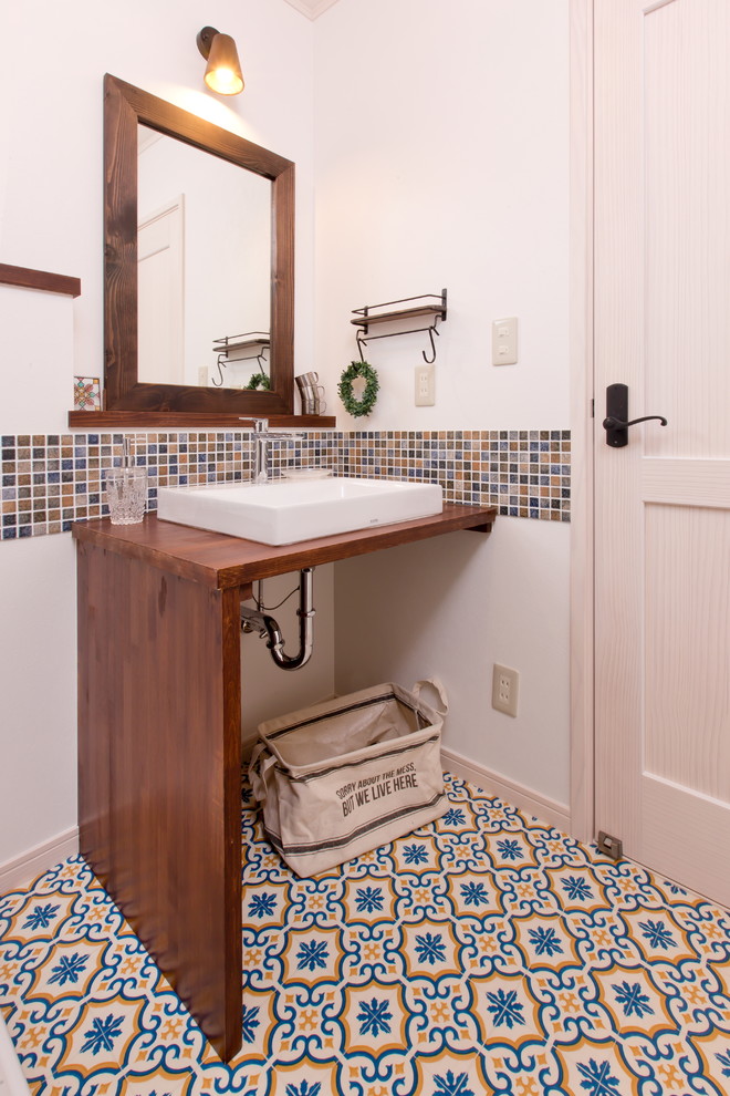 Foto på ett lantligt toalett, med vita väggar, ett fristående handfat, öppna hyllor, flerfärgad kakel, mosaik, vinylgolv, träbänkskiva och flerfärgat golv