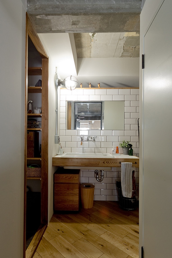 Exemple d'un WC et toilettes industriel avec un carrelage blanc, un mur blanc, un sol en bois brun, un lavabo encastré, un plan de toilette en carrelage et un sol beige.