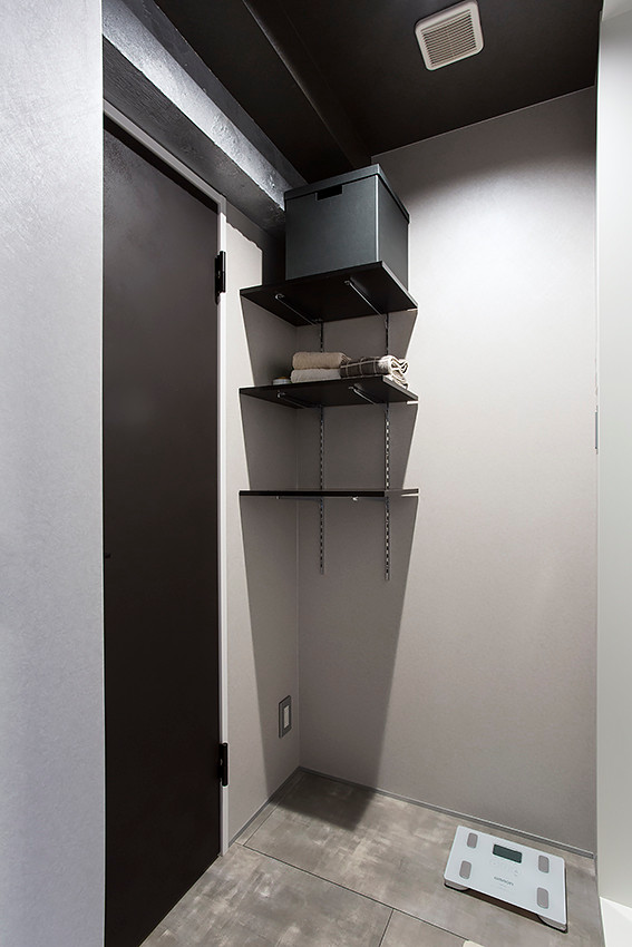 Bild på ett litet funkis grå grått toalett, med öppna hyllor, svarta skåp, grå väggar, vinylgolv, bänkskiva i rostfritt stål och grått golv