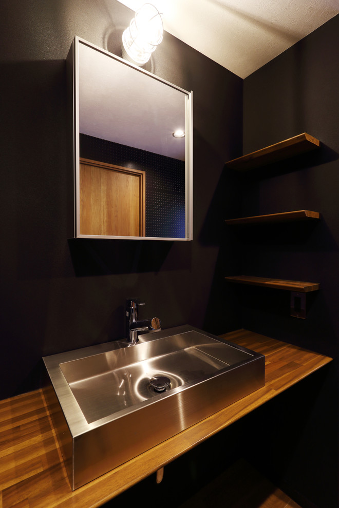 Cette image montre un WC et toilettes minimaliste en bois brun de taille moyenne avec un mur noir, un sol en bois brun, une vasque et un sol marron.