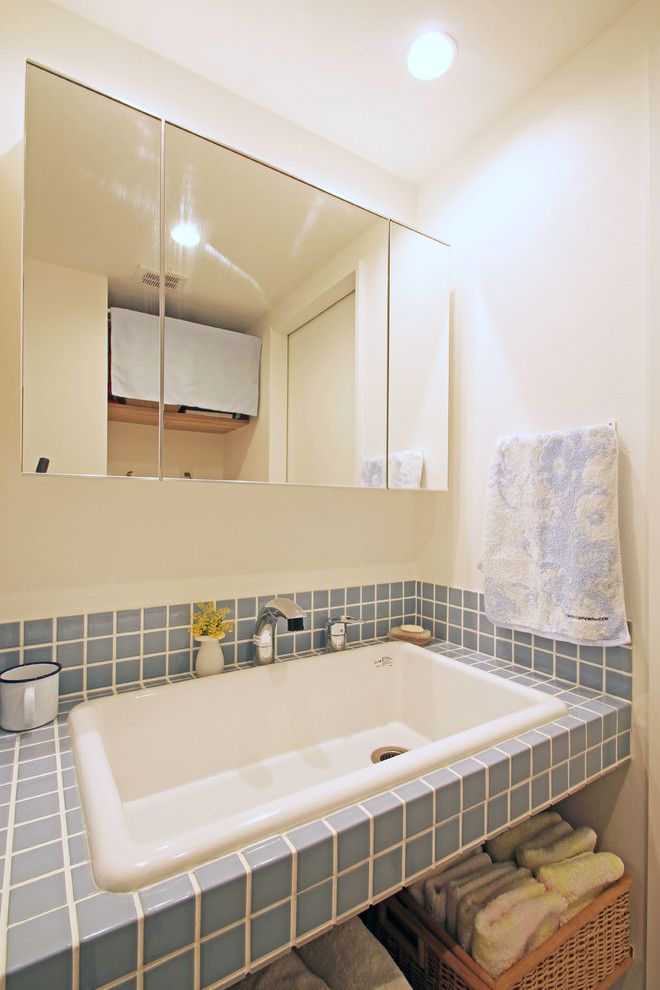 横浜にある北欧スタイルのおしゃれなトイレ・洗面所 (オープンシェルフ、青いタイル、磁器タイル、白い壁、クッションフロア、オーバーカウンターシンク、タイルの洗面台、白い床) の写真