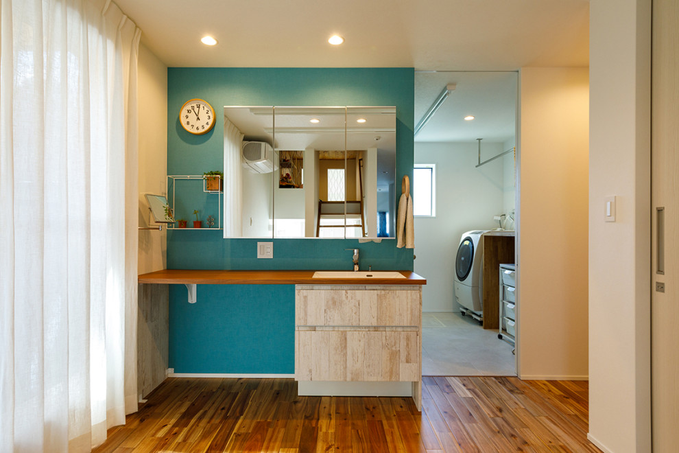 Foto på ett stort industriellt brun toalett, med blå väggar, ljust trägolv, brunt golv, öppna hyllor, beige skåp, ett undermonterad handfat och träbänkskiva