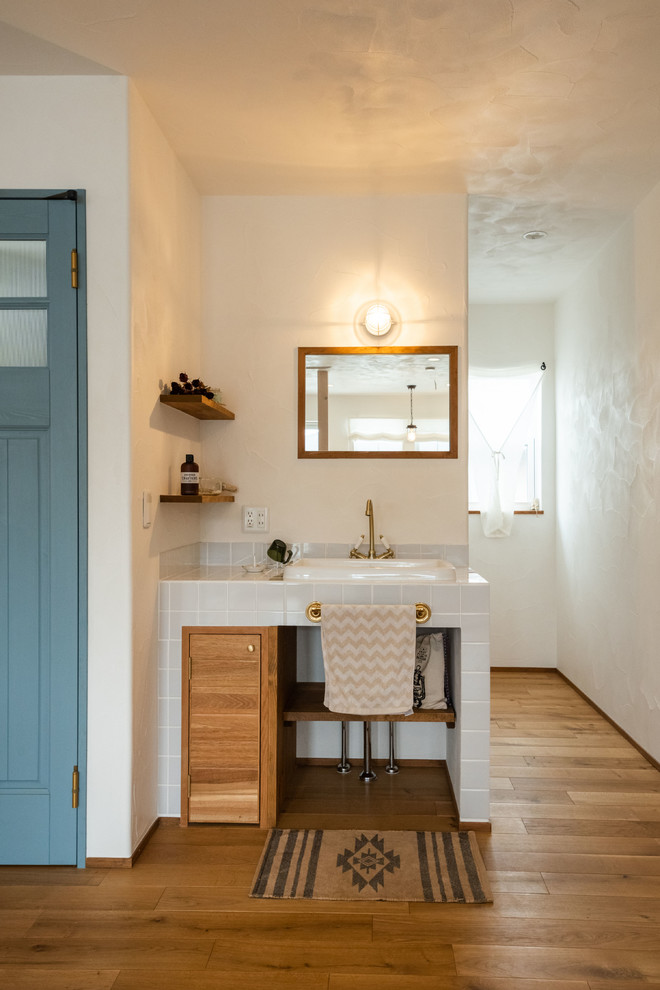 Cette photo montre un WC et toilettes nature en bois brun avec un carrelage blanc, un mur blanc, parquet clair, un plan de toilette en carrelage, un sol beige, un plan de toilette blanc, un placard à porte plane et un lavabo posé.