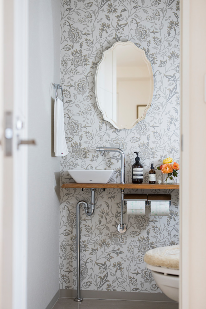 Moderne Gästetoilette mit grauer Wandfarbe, Aufsatzwaschbecken, Waschtisch aus Holz, grauem Boden, brauner Waschtischplatte und Tapetenwänden in Sonstige