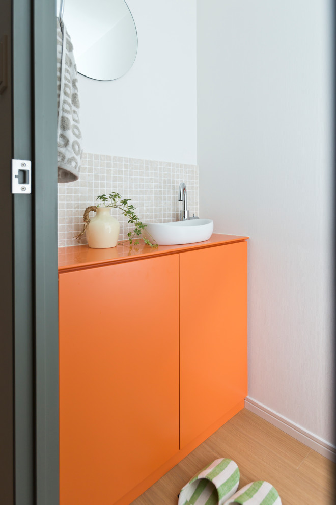 Réalisation d'un WC et toilettes design avec un placard à porte plane, des portes de placard oranges, un carrelage beige, mosaïque, un mur blanc, un sol en bois brun, une vasque, un sol marron, un plan de toilette beige et meuble-lavabo encastré.