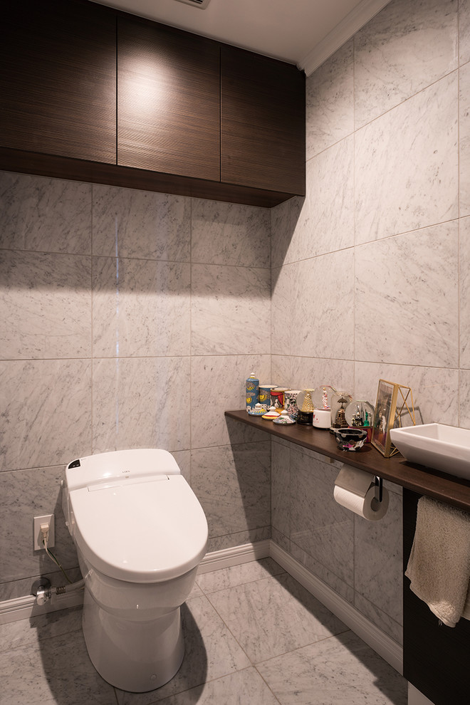 Стильный дизайн: туалет в современном стиле с серой плиткой, мраморной плиткой, серыми стенами, мраморным полом, настольной раковиной, столешницей из дерева, серым полом и коричневой столешницей - последний тренд