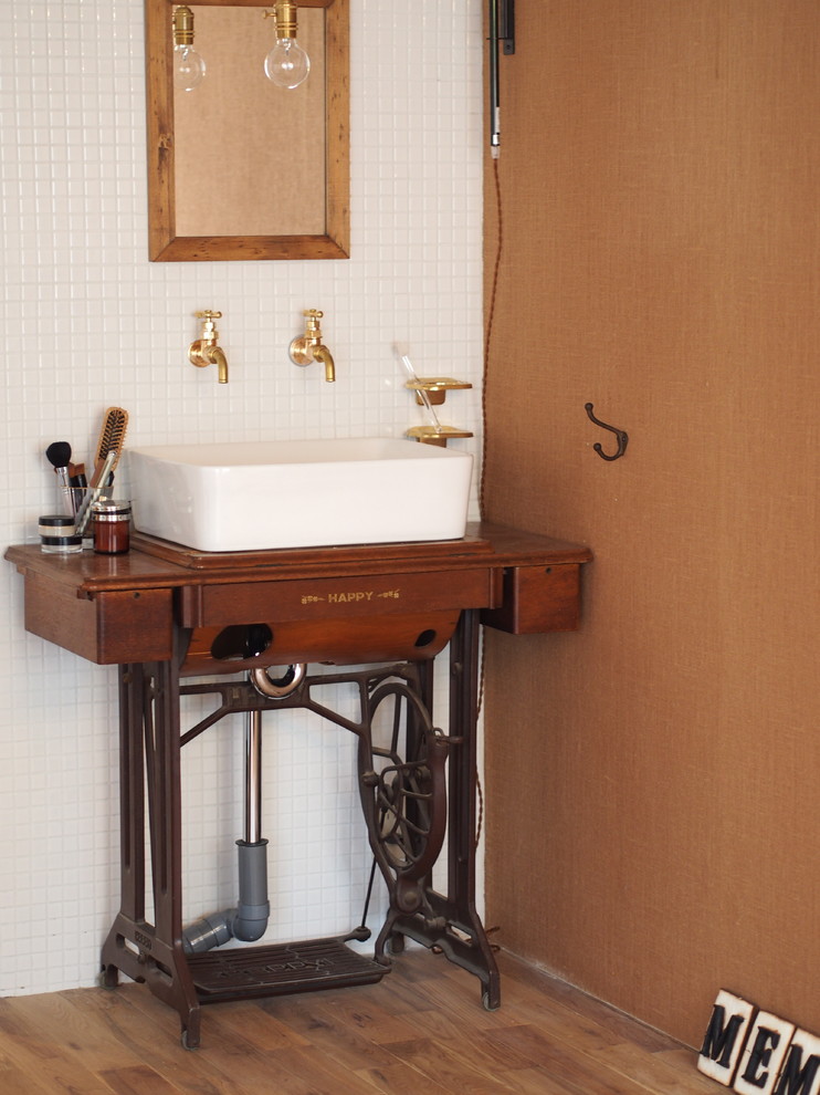 Inredning av ett rustikt litet brun brunt toalett, med skåp i mörkt trä, vit kakel, mellanmörkt trägolv, ett fristående handfat, träbänkskiva och bruna väggar
