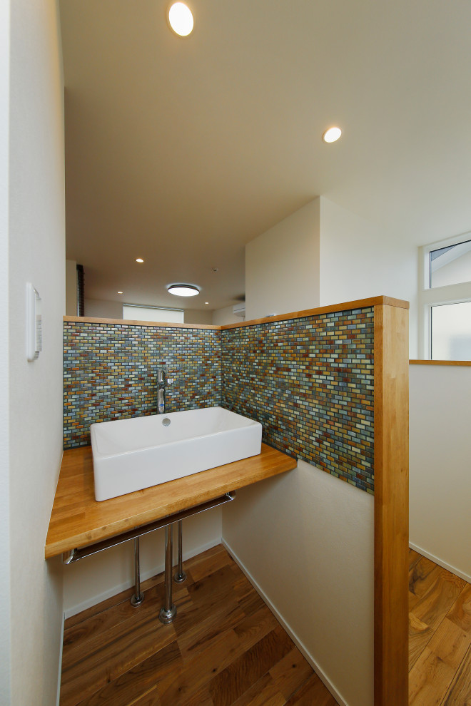 Bild på ett mellanstort funkis brun brunt toalett, med öppna hyllor, vita skåp, flerfärgad kakel, mosaik, vita väggar, mörkt trägolv, ett nedsänkt handfat, bänkskiva i zink och brunt golv