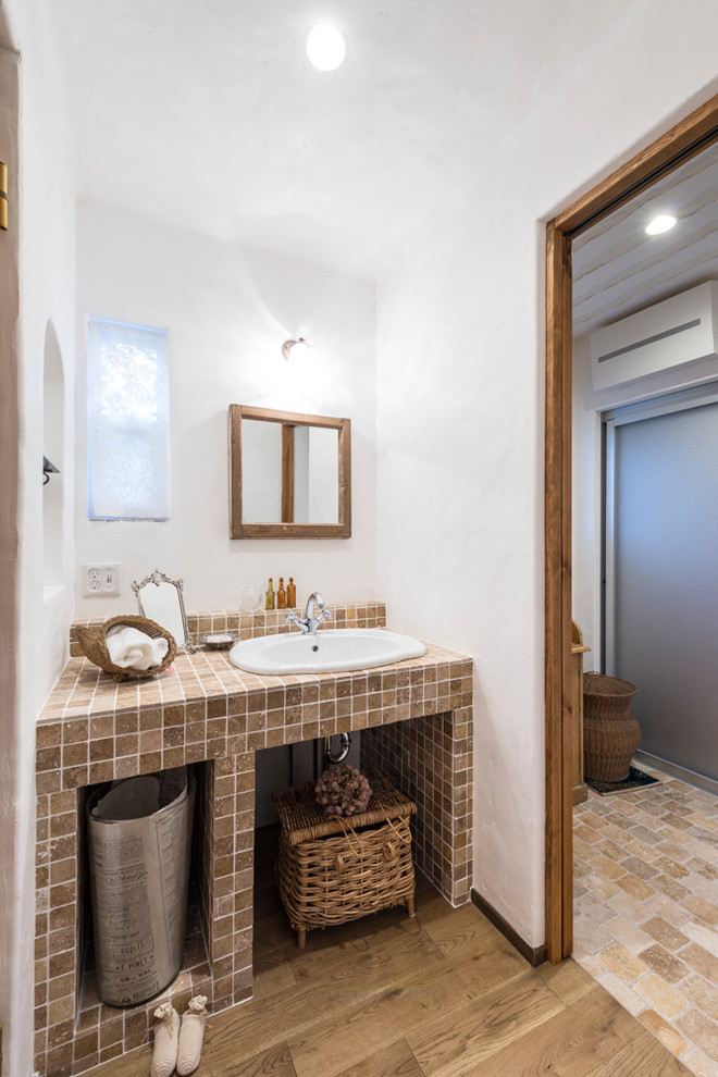 Kleine Mediterrane Gästetoilette mit braunen Fliesen, Steinfliesen, weißer Wandfarbe, hellem Holzboden, gefliestem Waschtisch, braunem Boden, beiger Waschtischplatte und Einbauwaschbecken in Fukuoka