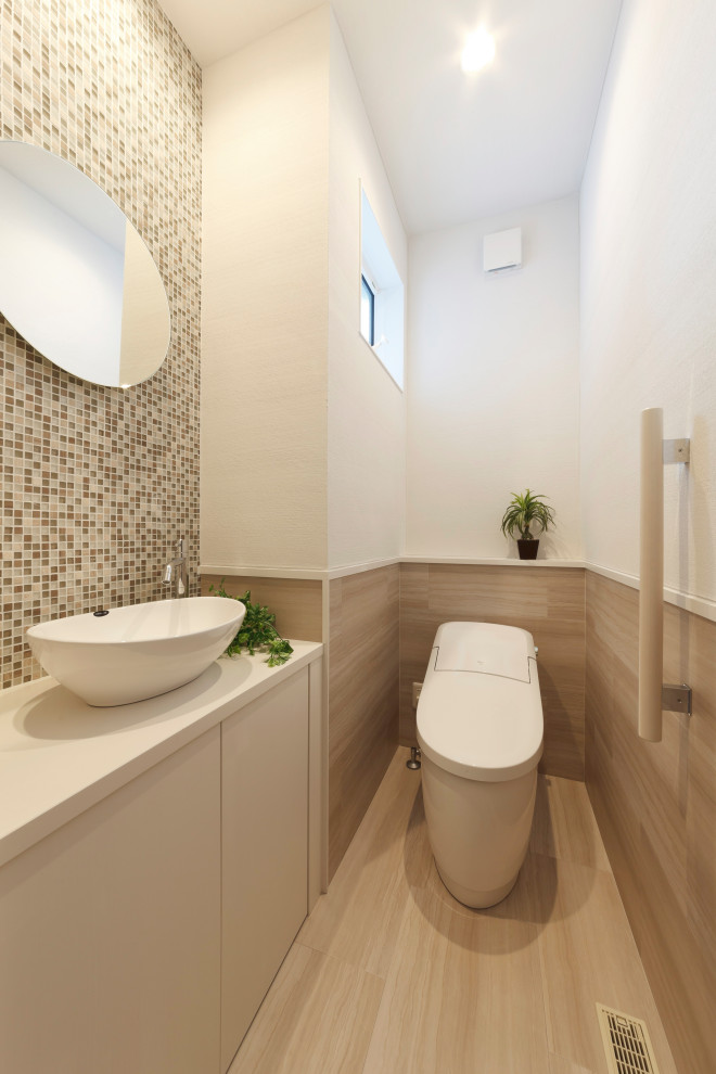 Bild på ett vit vitt toalett, med vita skåp, en toalettstol med hel cisternkåpa, flerfärgad kakel, glaskakel, beige väggar och träbänkskiva