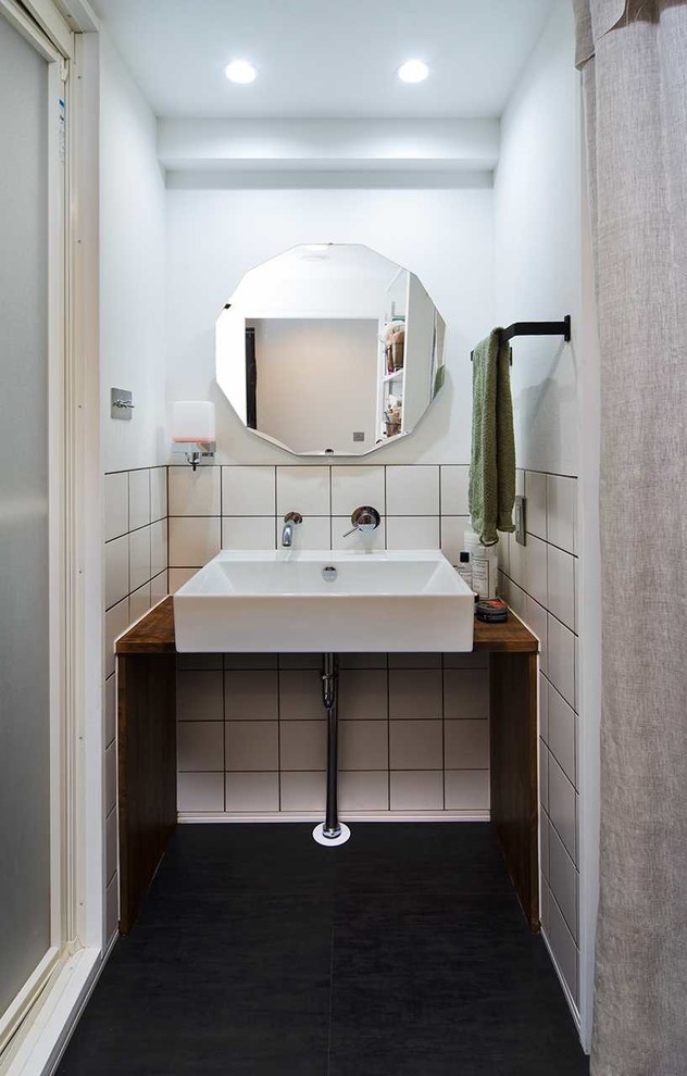 他の地域にあるインダストリアルスタイルのおしゃれなトイレ・洗面所 (白い壁、ベッセル式洗面器、木製洗面台、黒い床) の写真