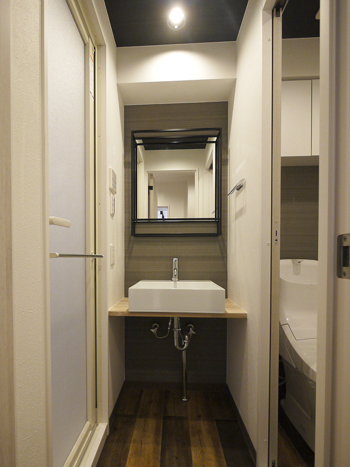 東京23区にあるラスティックスタイルのおしゃれなトイレ・洗面所 (一体型トイレ	、白い壁、セラミックタイルの床、ベッセル式洗面器、茶色い床、ベージュのカウンター) の写真