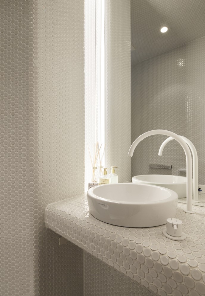 高級な中くらいなおしゃれなトイレ・洗面所 (白い壁、ベッセル式洗面器、タイルの洗面台、グレーのタイル) の写真