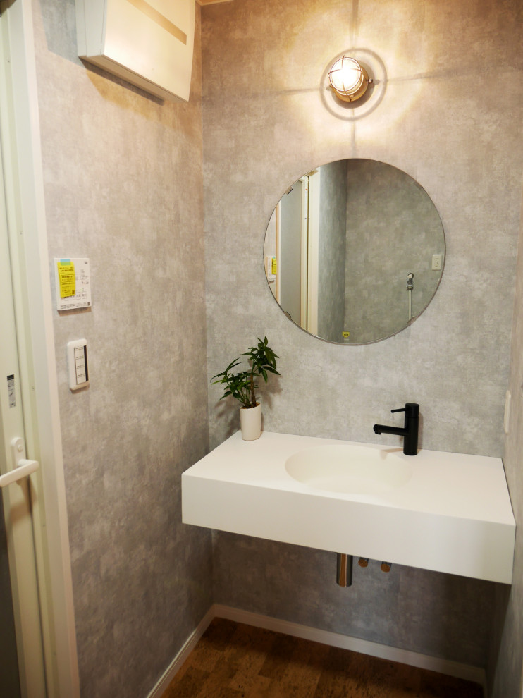 Inredning av ett modernt litet vit vitt toalett, med öppna hyllor, vita skåp, en toalettstol med separat cisternkåpa, grå väggar, vinylgolv, ett väggmonterat handfat och brunt golv