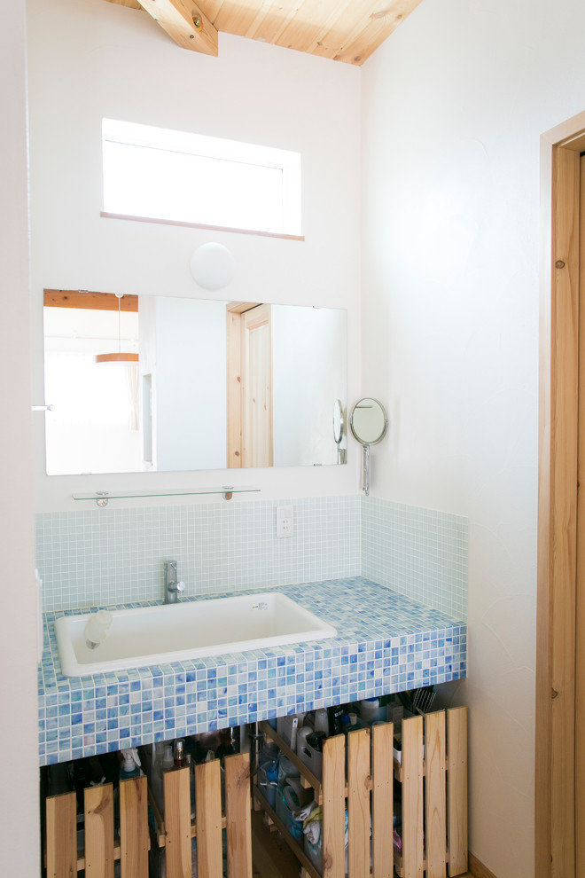 Inspiration för ett blå blått toalett, med öppna hyllor, blå kakel, porslinskakel, vita väggar, mellanmörkt trägolv, ett avlångt handfat, kaklad bänkskiva och brunt golv