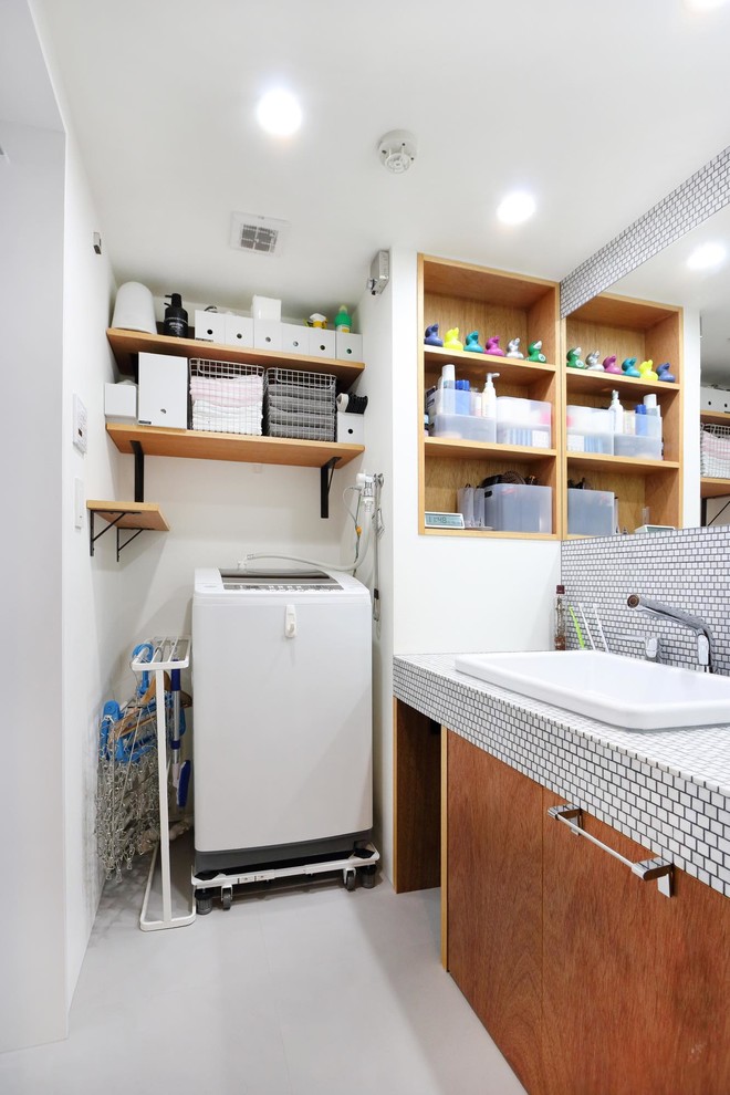 東京23区にあるインダストリアルスタイルのおしゃれなトイレ・洗面所 (フラットパネル扉のキャビネット、中間色木目調キャビネット、白い壁、オーバーカウンターシンク、グレーの床、白い洗面カウンター) の写真