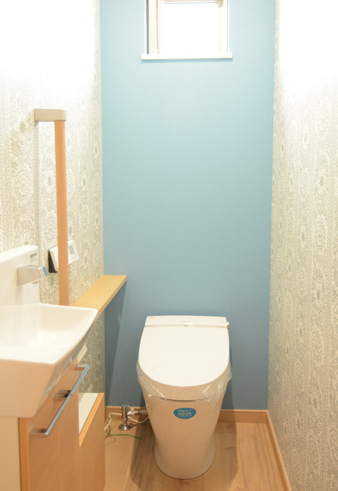Idée de décoration pour un WC et toilettes avec des portes de placard beiges, WC à poser, un mur bleu, un sol en vinyl et un sol beige.