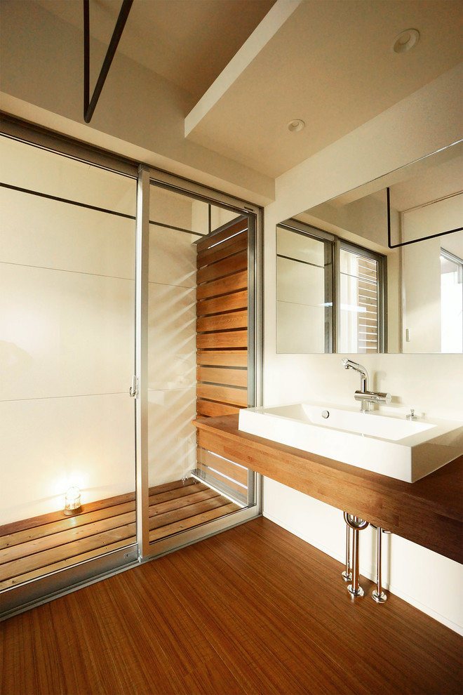 Diseño de aseo de estilo zen con paredes blancas, lavabo sobreencimera y encimera de madera