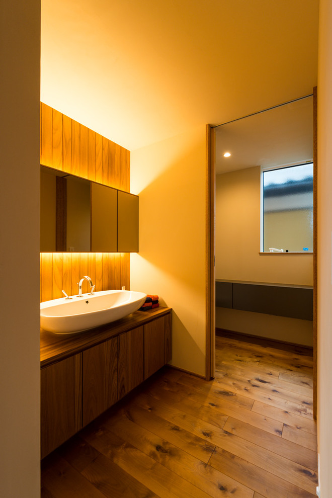 Modern inredning av ett brun brunt toalett, med släta luckor, skåp i mellenmörkt trä, beige väggar, mellanmörkt trägolv, ett fristående handfat, träbänkskiva och brunt golv