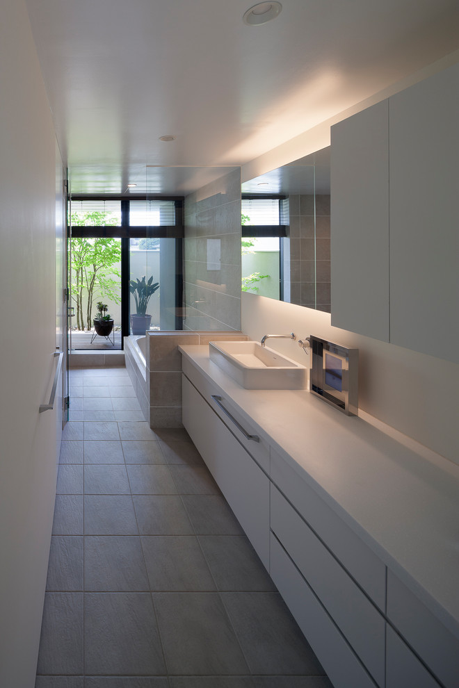 他の地域にあるコンテンポラリースタイルのおしゃれなトイレ・洗面所 (フラットパネル扉のキャビネット、白いキャビネット、白い壁、ベッセル式洗面器、グレーの床、白い洗面カウンター) の写真