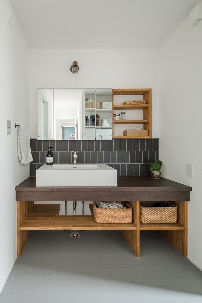 Design ideas for a large world-inspired cloakroom in Other with open cabinets, beige cabinets, a two-piece toilet, black tiles, porcelain tiles, white walls, vinyl flooring, a built-in sink, wooden worktops, grey floors and brown worktops.