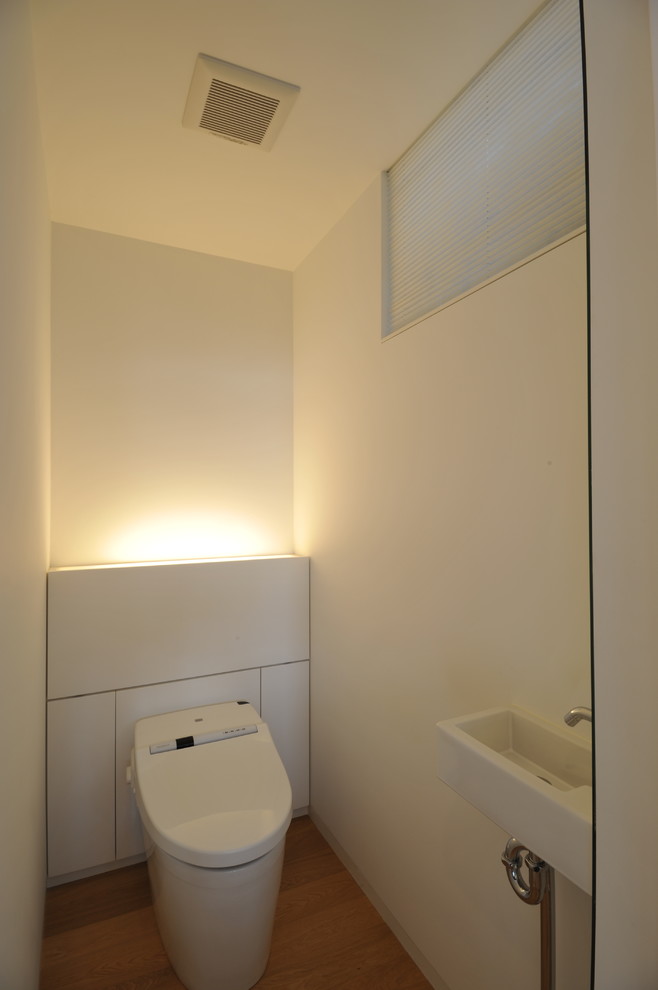 На фото: маленький туалет в современном стиле с плоскими фасадами, белыми фасадами, унитазом-моноблоком, белыми стенами, полом из фанеры, подвесной раковиной и коричневым полом для на участке и в саду с