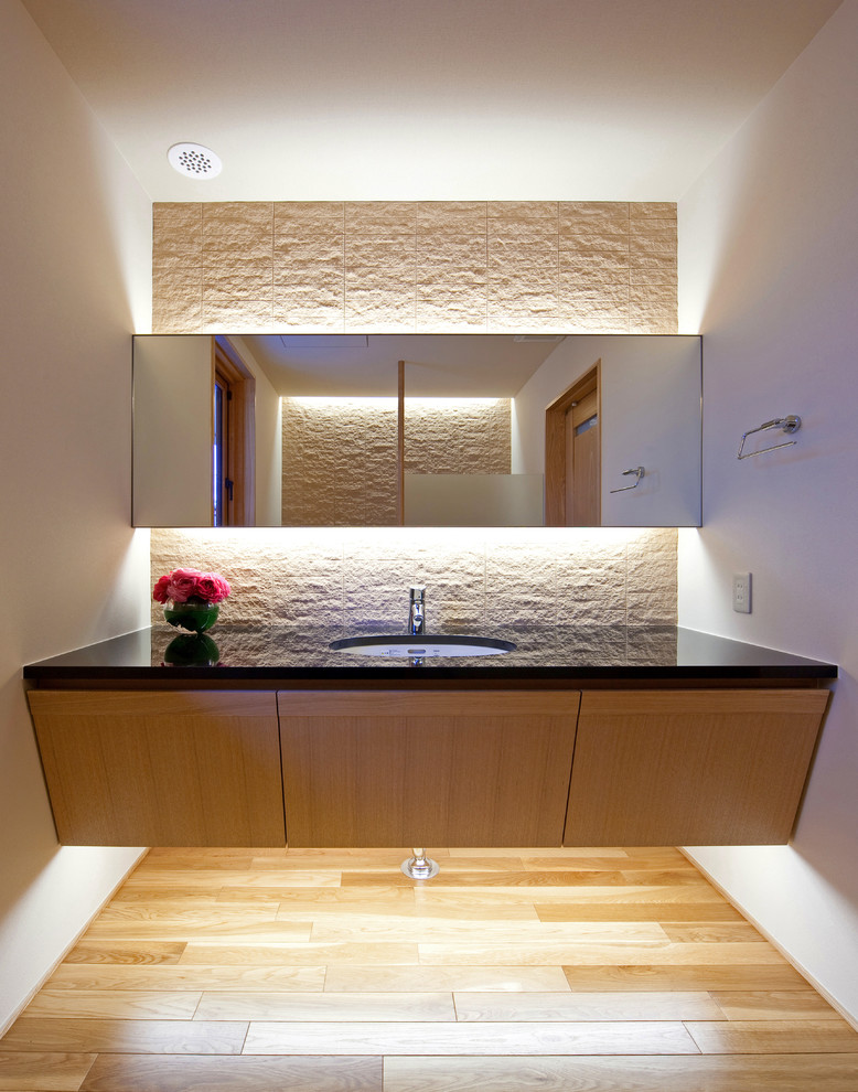 Réalisation d'un WC et toilettes design en bois clair avec un placard à porte plane, un carrelage beige, un mur beige, parquet clair, un lavabo encastré et un sol beige.
