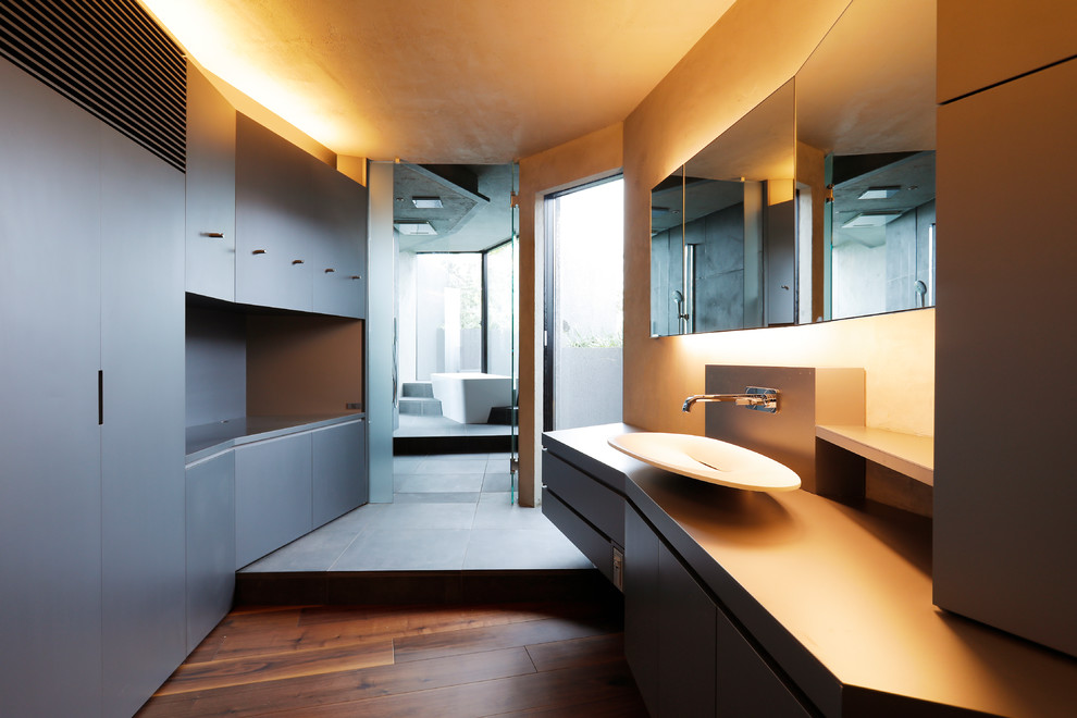 東京23区にある中くらいなインダストリアルスタイルのおしゃれなトイレ・洗面所 (フラットパネル扉のキャビネット、グレーのキャビネット、白い壁、濃色無垢フローリング、ベッセル式洗面器、茶色い床) の写真