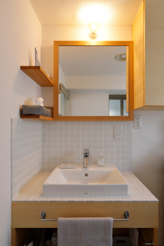 This is an example of a cloakroom in Nagoya with open cabinets, white cabinets, white tiles, porcelain tiles, white walls, a vessel sink, tiled worktops, white worktops, a built in vanity unit, a wallpapered ceiling and wallpapered walls.