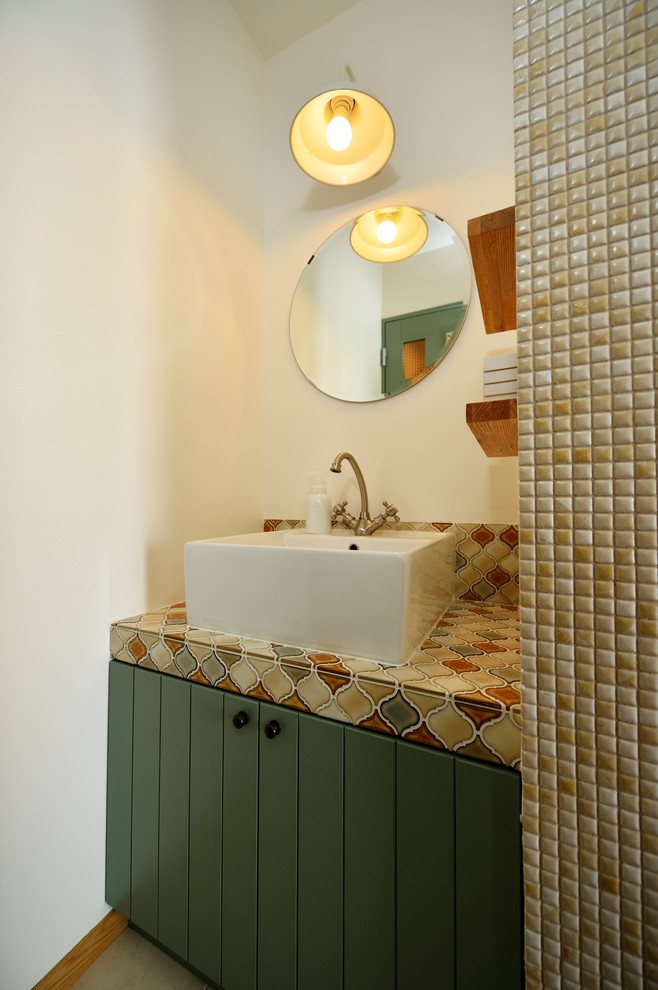 他の地域にある地中海スタイルのおしゃれなトイレ・洗面所 (家具調キャビネット、緑のキャビネット、白い壁、ベッセル式洗面器、グレーの床) の写真