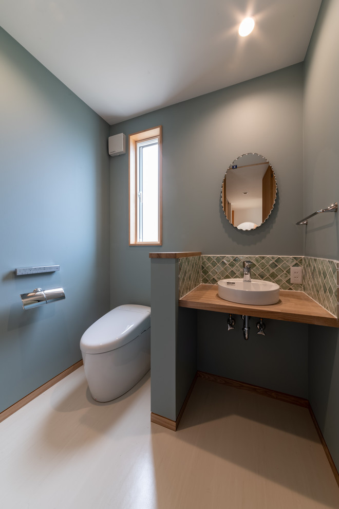 Powder room - mid-sized scandinavian green tile and porcelain tile linoleum floor, beige floor, wallpaper ceiling and wallpaper powder room idea in Other with a one-piece toilet, blue walls, a vessel sink, wood countertops, open cabinets, medium tone wood cabinets, brown countertops and a built-in vanity