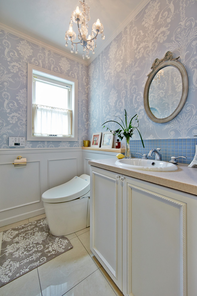 Klassisk inredning av ett toalett, med luckor med infälld panel, vita skåp, blå kakel, blå väggar, marmorgolv, ett nedsänkt handfat och beiget golv
