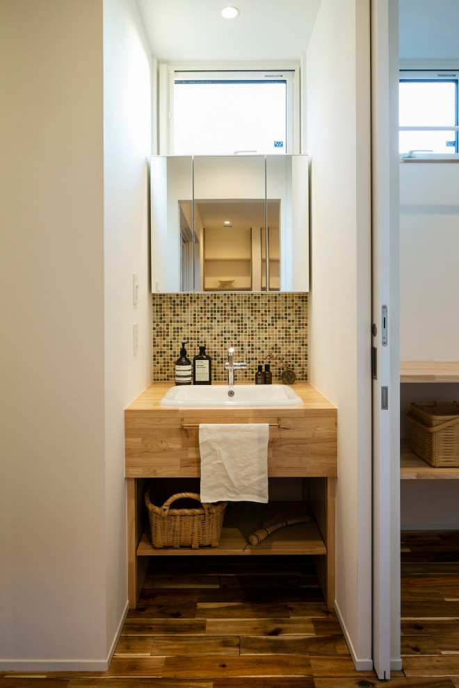 Rustik inredning av ett litet brun brunt toalett, med öppna hyllor, vita skåp, mosaik, vita väggar, mellanmörkt trägolv, ett undermonterad handfat, träbänkskiva och brunt golv