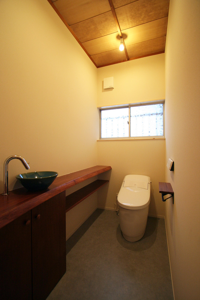 Asiatische Gästetoilette mit beiger Wandfarbe, Betonboden, Aufsatzwaschbecken und grauem Boden in Sonstige