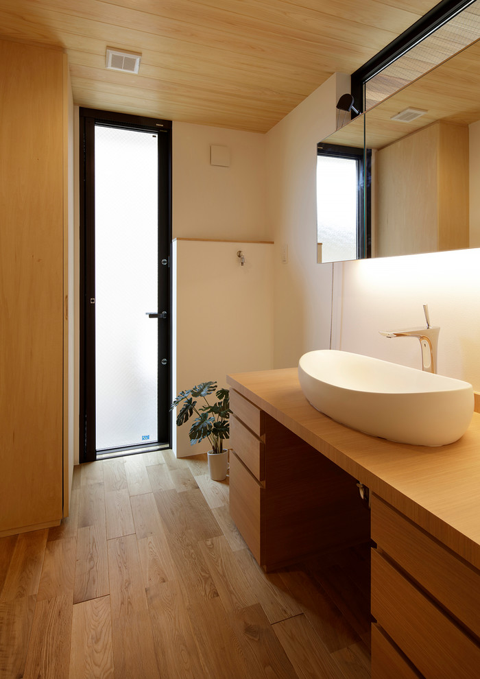 Пример оригинального дизайна: туалет в стиле модернизм с плоскими фасадами, коричневыми фасадами, белыми стенами, паркетным полом среднего тона, настольной раковиной, столешницей из дерева, коричневым полом и коричневой столешницей