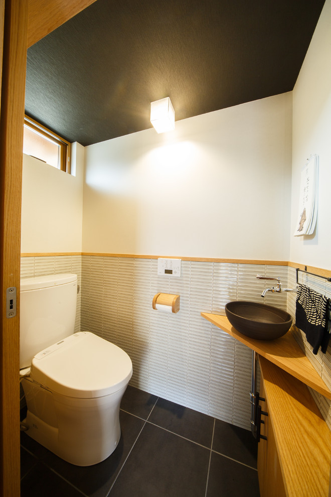 京都にある中くらいな和風のおしゃれなトイレ・洗面所 (フラットパネル扉のキャビネット、中間色木目調キャビネット、白い壁、ベッセル式洗面器、木製洗面台、黒い床) の写真