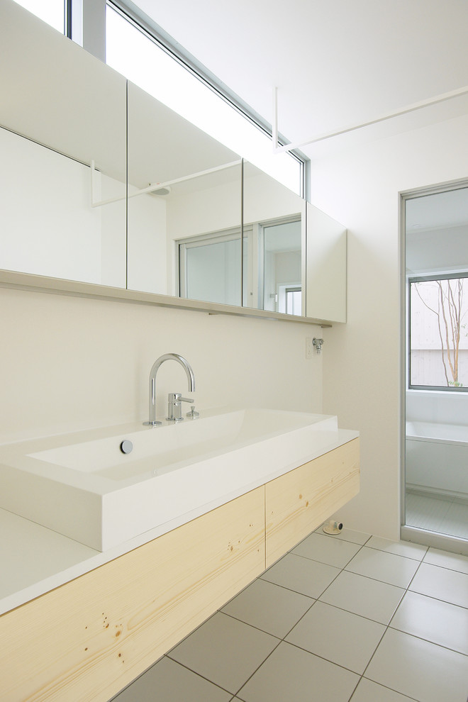 Exemple d'un WC et toilettes moderne en bois clair avec un placard à porte plane, un mur blanc, une vasque et un sol gris.