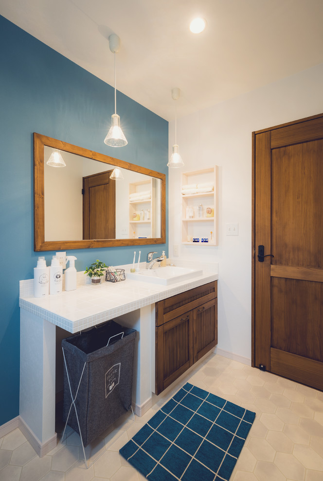 他の地域にあるカントリー風のおしゃれなトイレ・洗面所 (中間色木目調キャビネット、青い壁、オーバーカウンターシンク、タイルの洗面台、ベージュの床) の写真