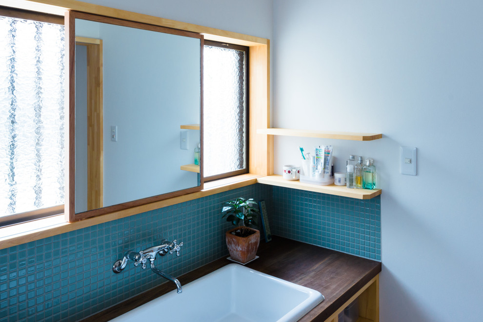 京都にある小さな北欧スタイルのおしゃれなトイレ・洗面所 (青いタイル、モザイクタイル、白い壁、オーバーカウンターシンク、木製洗面台、黒い洗面カウンター) の写真
