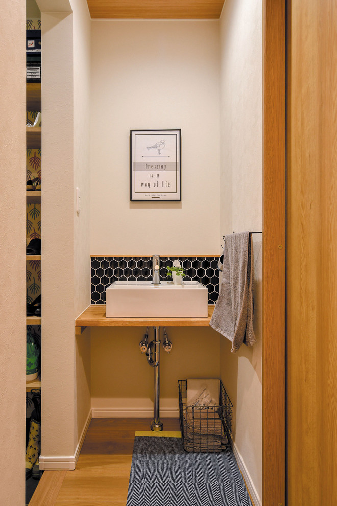Esempio di un piccolo bagno di servizio scandinavo con piastrelle nere, piastrelle in gres porcellanato, pareti bianche, pavimento in legno massello medio, lavabo da incasso, top in legno, pavimento marrone e top marrone