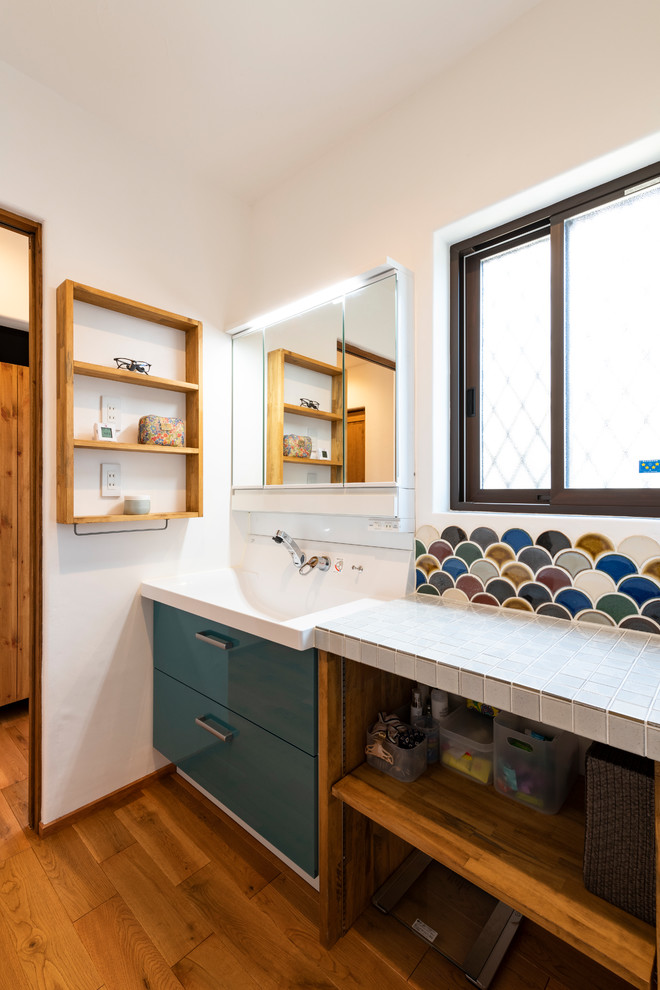 Example of a mid-sized country white tile and porcelain tile dark wood floor and brown floor powder room design in Other with flat-panel cabinets, blue cabinets, a one-piece toilet, white walls, an undermount sink, solid surface countertops and red countertops