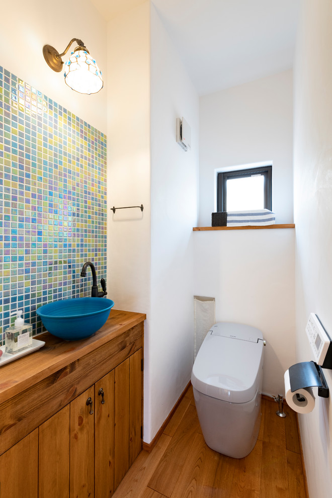Medium sized rural cloakroom in Other with freestanding cabinets, a one-piece toilet, multi-coloured tiles, mosaic tiles, white walls, dark hardwood flooring, a submerged sink, wooden worktops, brown floors and blue worktops.