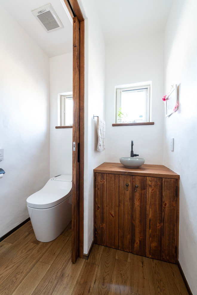 Kleine Mediterrane Gästetoilette mit braunen Schränken, Toilette mit Aufsatzspülkasten, weißer Wandfarbe, dunklem Holzboden, Einbauwaschbecken, Waschtisch aus Holz, braunem Boden und brauner Waschtischplatte in Sonstige