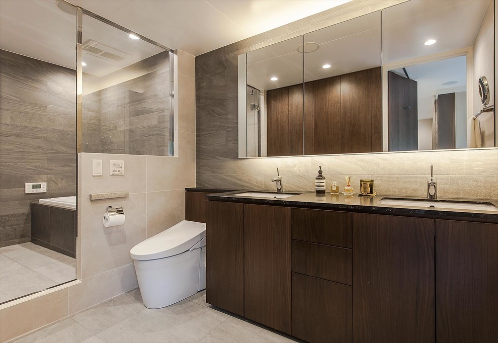 This is an example of a modern cloakroom with flat-panel cabinets, dark wood cabinets, grey tiles, beige walls, beige floors and black worktops.