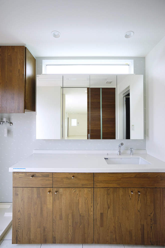 Inspiration för stora moderna vitt toaletter, med luckor med profilerade fronter, skåp i mörkt trä, vita väggar, vinylgolv, bänkskiva i akrylsten, ett undermonterad handfat och vitt golv