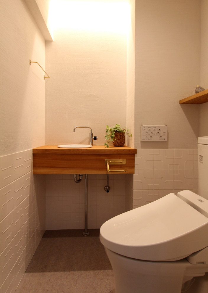 Aménagement d'un petit WC et toilettes moderne avec un carrelage blanc, des carreaux de porcelaine, un mur blanc, un sol en linoléum, un lavabo posé, un plan de toilette en bois, un sol gris et un plan de toilette marron.