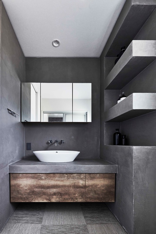 Bild på ett industriellt toalett, med släta luckor, bruna skåp, grå väggar, ett fristående handfat, bänkskiva i betong och grått golv