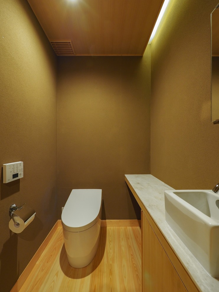 Идея дизайна: туалет в восточном стиле с светлыми деревянными фасадами, коричневыми стенами, настольной раковиной, коричневым полом, плоскими фасадами и светлым паркетным полом