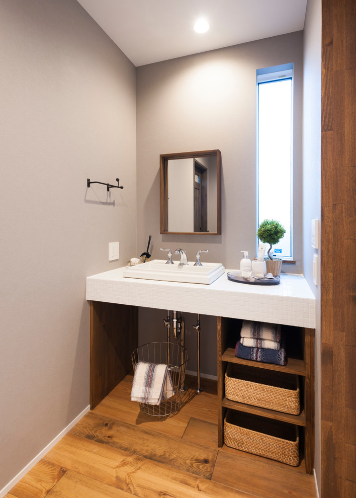 Skandinavische Gästetoilette mit offenen Schränken, grauer Wandfarbe, braunem Holzboden, Einbauwaschbecken, braunem Boden und weißer Waschtischplatte in Sonstige
