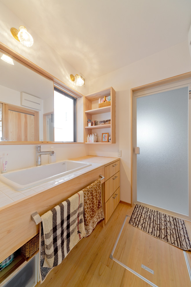 На фото: туалет в восточном стиле с плоскими фасадами, светлыми деревянными фасадами, белыми стенами, светлым паркетным полом, настольной раковиной и бежевым полом с